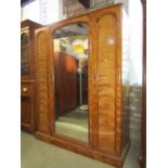 A Victorian satin birch wardrobe enclosed by three arched panelled doors, the central with mirror