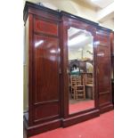 A good quality Edwardian mahogany breakfront wardrobe enclosed by a central mirror panelled door