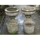 A pair of weathered cast composition stone garden urns, the squat circular bowls raised on loose