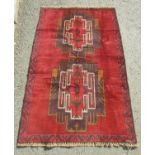 A Baluchi rug with two central motifs and continuous hook border in deep tones of crimson, wine,