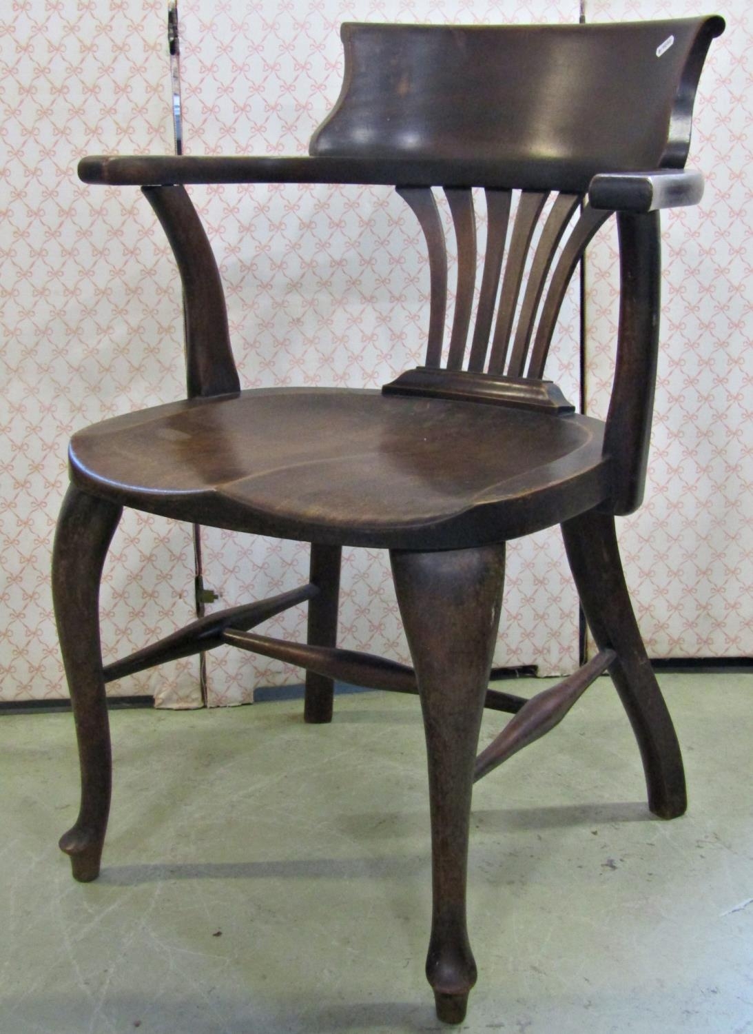 An early 20th century walnut office desk chair with combed splat over a saddle shaped seat