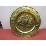 A 19th century armorial dish in brass with repeating scrolled borders, to the centre a heraldic