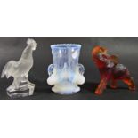 A Nachmann frosted glass cockerel 11cm, a Vaseline glass beaker with three swan handles, and amber