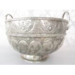 A large silver metal Middle Eastern twin handled punch bowl with an embossed and engraved foliate