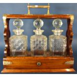 An early 20th century oak three bottle tantalus with a hinged front panel and lock, complete with