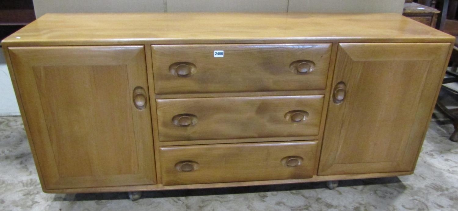 An Ercol light elm low sideboard enclosed by two doors flanking three drawers with oval dished