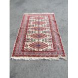 A Middle Eastern rug with a row of five diamond medallions on a red and white ground, 190cm x