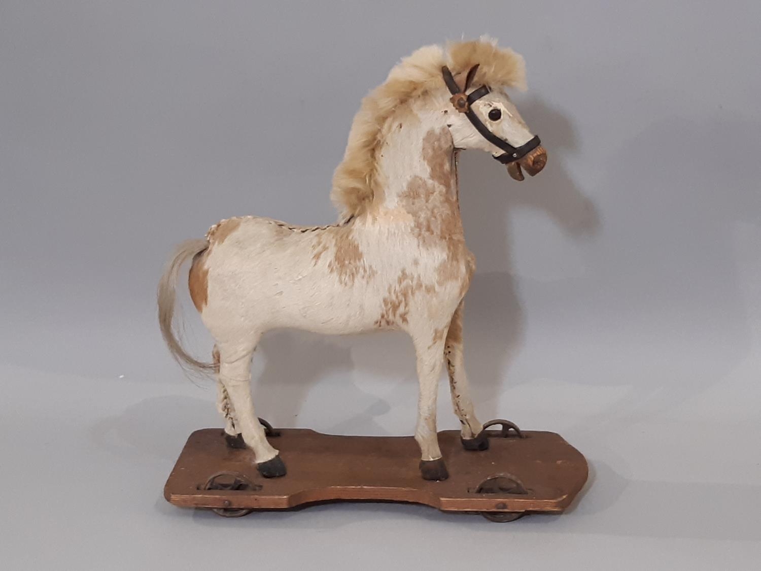 Pull along horse; a small pony skin horse, mounted on a pine base and with metal wheels to each