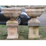 A pair of weathered cast composition stone square tapered garden urns, raised on loose socles and