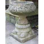 A weathered cast composition stone garden urn of circular form, raised on squat pedestal with