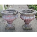 A pair of weathered cast composition stone garden urns, set on socles with square bases, 40 cm