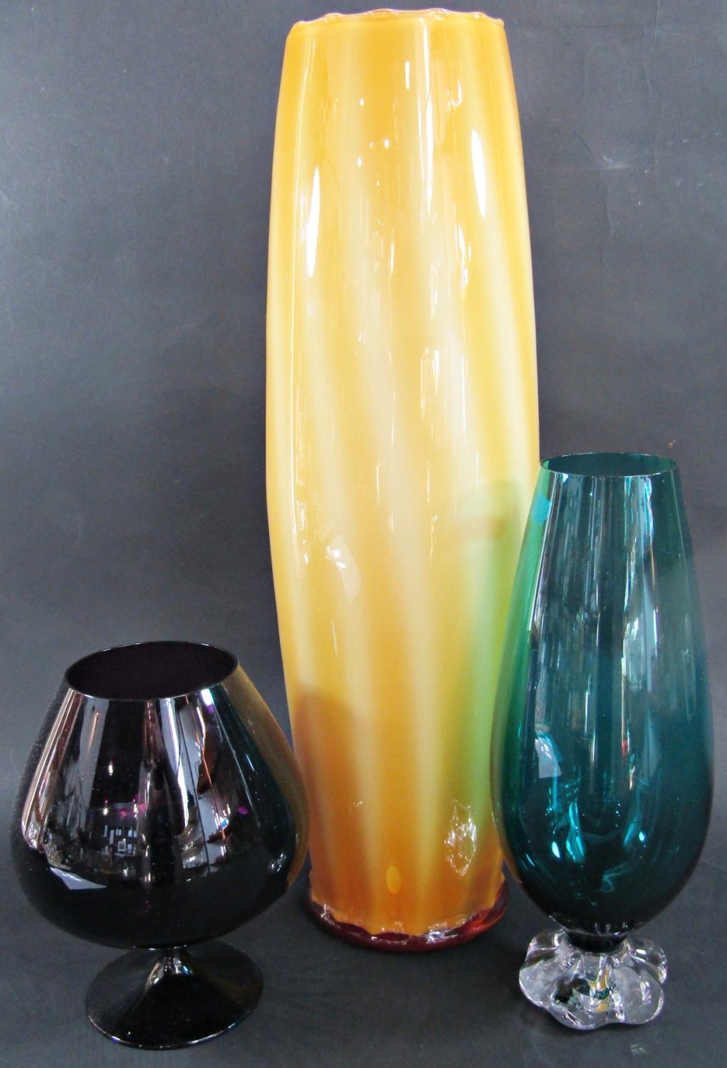 Three modern glass vessels, a tall yellow vase, 47cm, a green glass vase and a large purple brandy