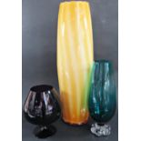 Three modern glass vessels, a tall yellow vase, 47cm, a green glass vase and a large purple brandy