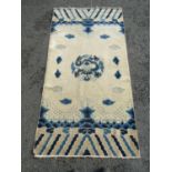 An antique Chinese blue and white rug with a central dragon symbol amongst clouds, 150cm x 79cm
