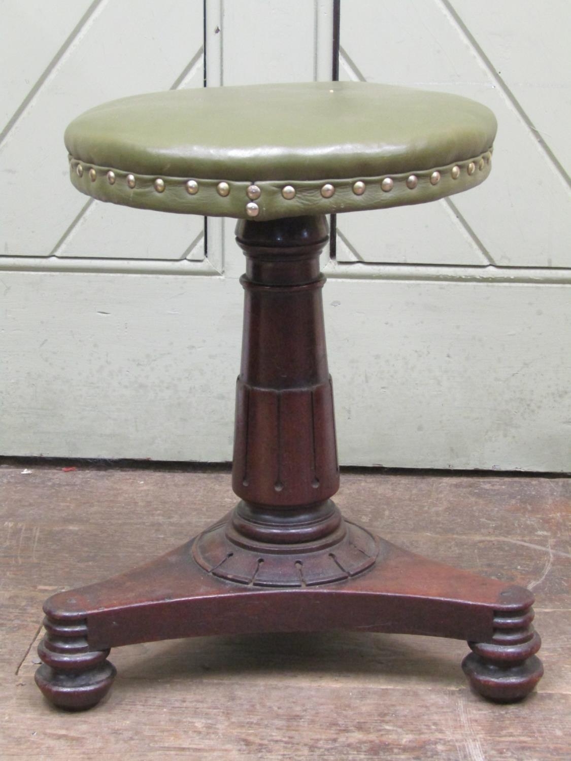 A William IV mahogany piano stool upholstered in green leather, raised on an adjustable column and