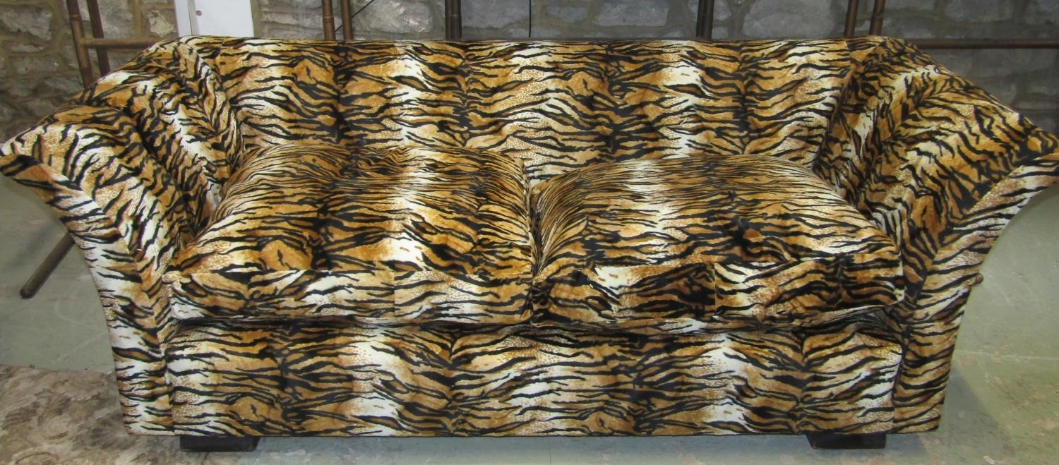 A two seat sofa with swept arms upholstered in a tiger print fabric with loose squab feather