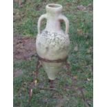 A small weathered buff coloured terracotta amphora with moulded loop handles and set on an iron work