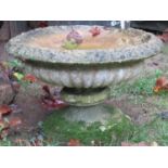 A weathered cast composition stone garden urn, 62 cm in diameter raised on an associated circular