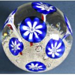 A single clear glass paperweight with seven stylised blue flowers emerging from a frothy, bubbly