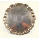 George V silver circular salver with hammered decoration and vacant cartouche, within a shaped