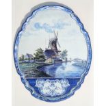 Dutch Delft shaped oval plaque painted with a river, 2 cattle, 2 windmills, buildings, trees and