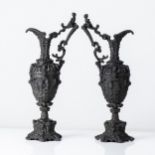 A PAIR OF METAL EWERS The baluster body raised on a shaped base and supporting an S-scroll handle