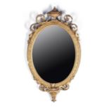 AN OVAL GILTWOOD MIRROR, LATE 19TH CENTURY Surmounted by an urn finial flanked by leaf-carved beaded