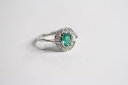 Platinum oval bezel set Emerald in a diamond surround with baguettes leading of the the shank. E0.