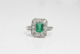 Platinum art deco inspired emerald and diamondring. The central emerald is in a rub over setting