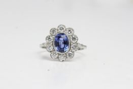 Platinum oval sapphire and diamond cluster ring.The oval sapphire is in a rub over setting with