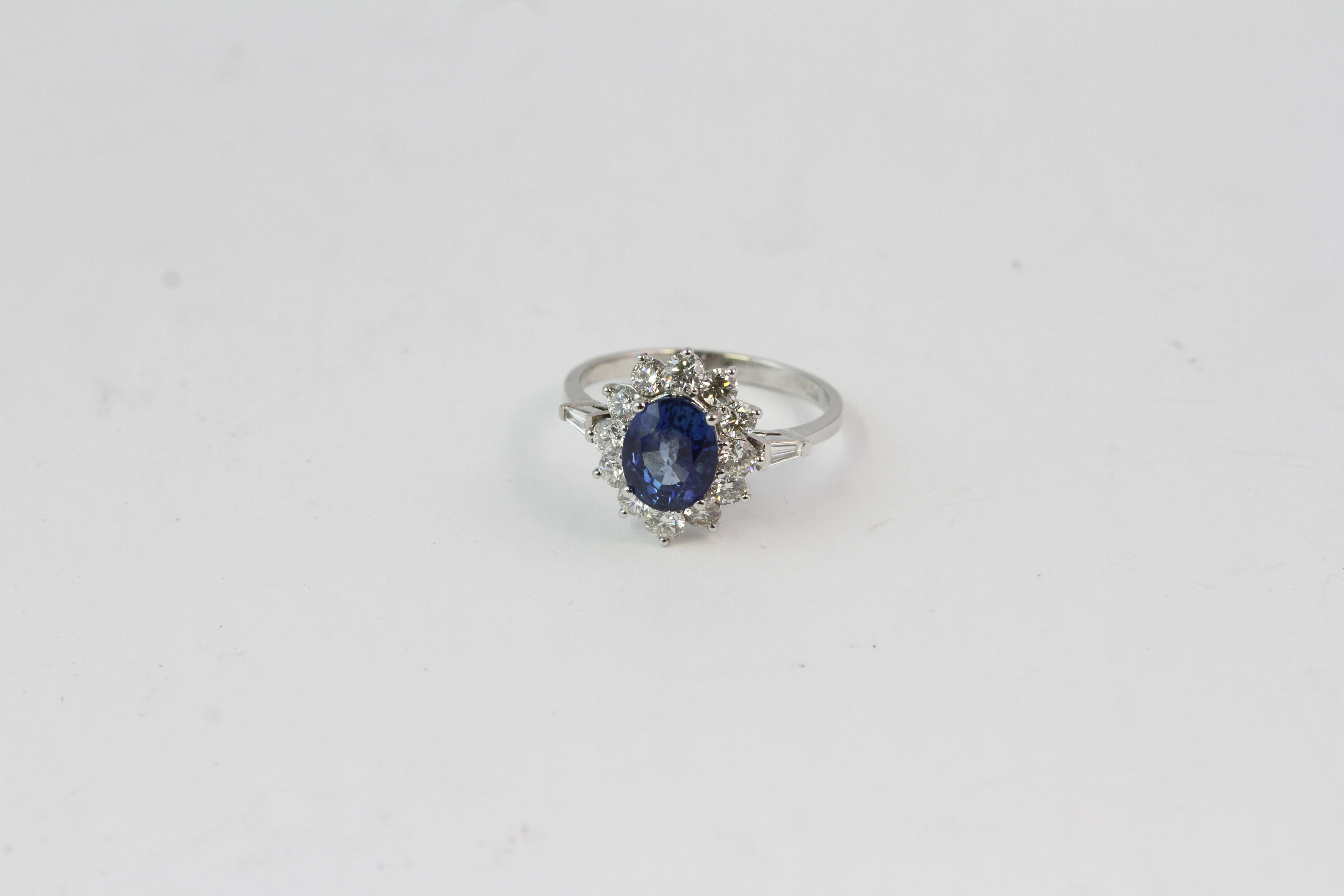 18WG oval sapphire and diamond cluster ring. S2.10 D0.85 with baguettes to the tip of the shoulder