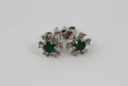 White gold a pair of star shaped earrings with round emerald centers and diamonds to each point.