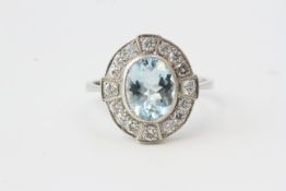Aqua and diamond ring. The centrally set mixed cut oval aquamarine is in a rub over setting