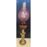 Brass oil lamp, cranberry shade and font with cherubs, approximate height 28 inches