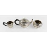 A white metal miniature tea set comprising teapot, sugar bowl and milk jug, all embossed with