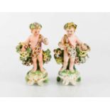 A pair of 18th century Derby porcelain cherub figurines, holding baskets of flowers, bearing old