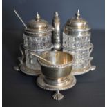 A Victorian three bottle cruet set with cut glass bottles and silver tops, raised on hoof feet,