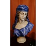 A pottery bust in the form of a woman wearing cap and blue dress.