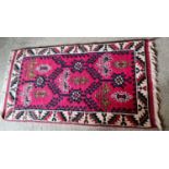 A small red ground antique Middle Eastern rug with cream ground border.