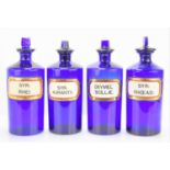 Four antique blue glass apothecary bottles with stoppers and bearing Latin labels, 25cm high.