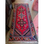 An antique Middle Eastern red ground rug, with quatreform motifs to the centre, and chevron border.