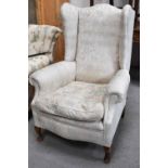 An antique wingback armchair, mahogany frame with pale coloured upholstery.