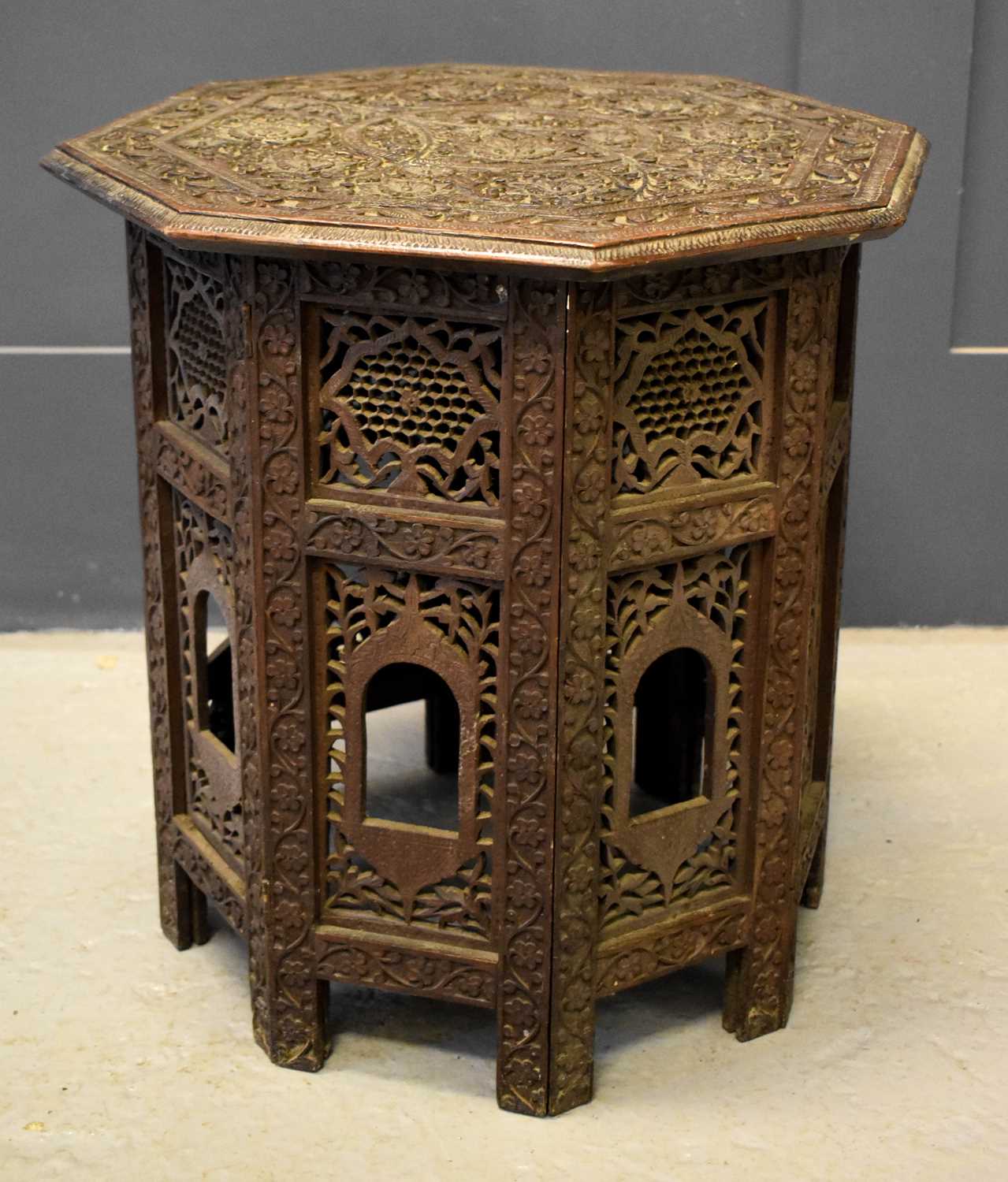 A small Indian carved table with folding base composed of pierced decorative panels and having an
