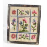 A silver table picture frame displaying an antique crewel work panel, 28 by 23cm.