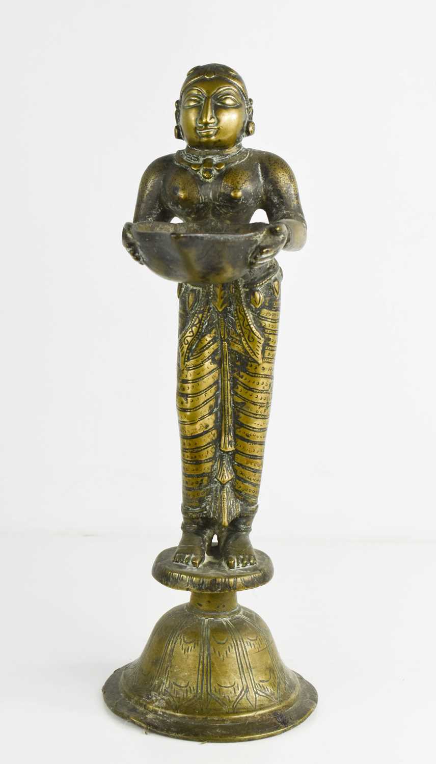 A 19th century Indonesian brass sculpture of a woman holding a bowl, raised on a bell form base,