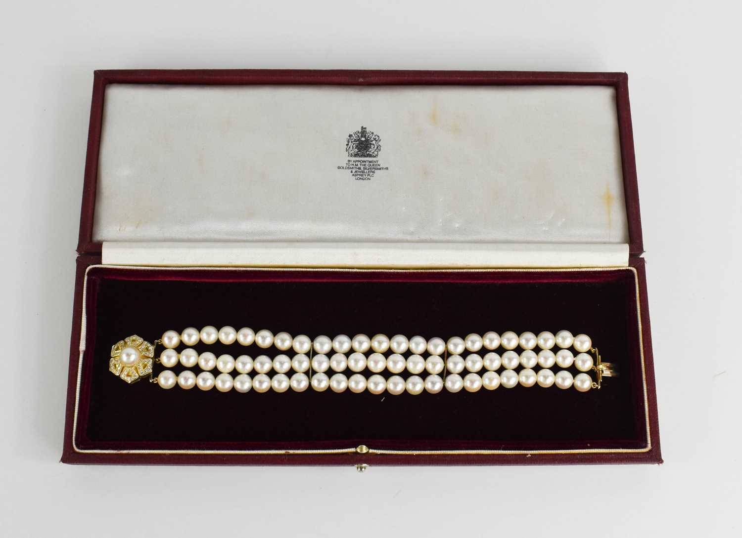An 18ct gold and three strand pearl bracelet, by Leo de Vroomen, London 1984, the strands gathered