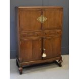 An early 20th century oak cabinet of Chinese influence with a large scroll work brass escutcheon and