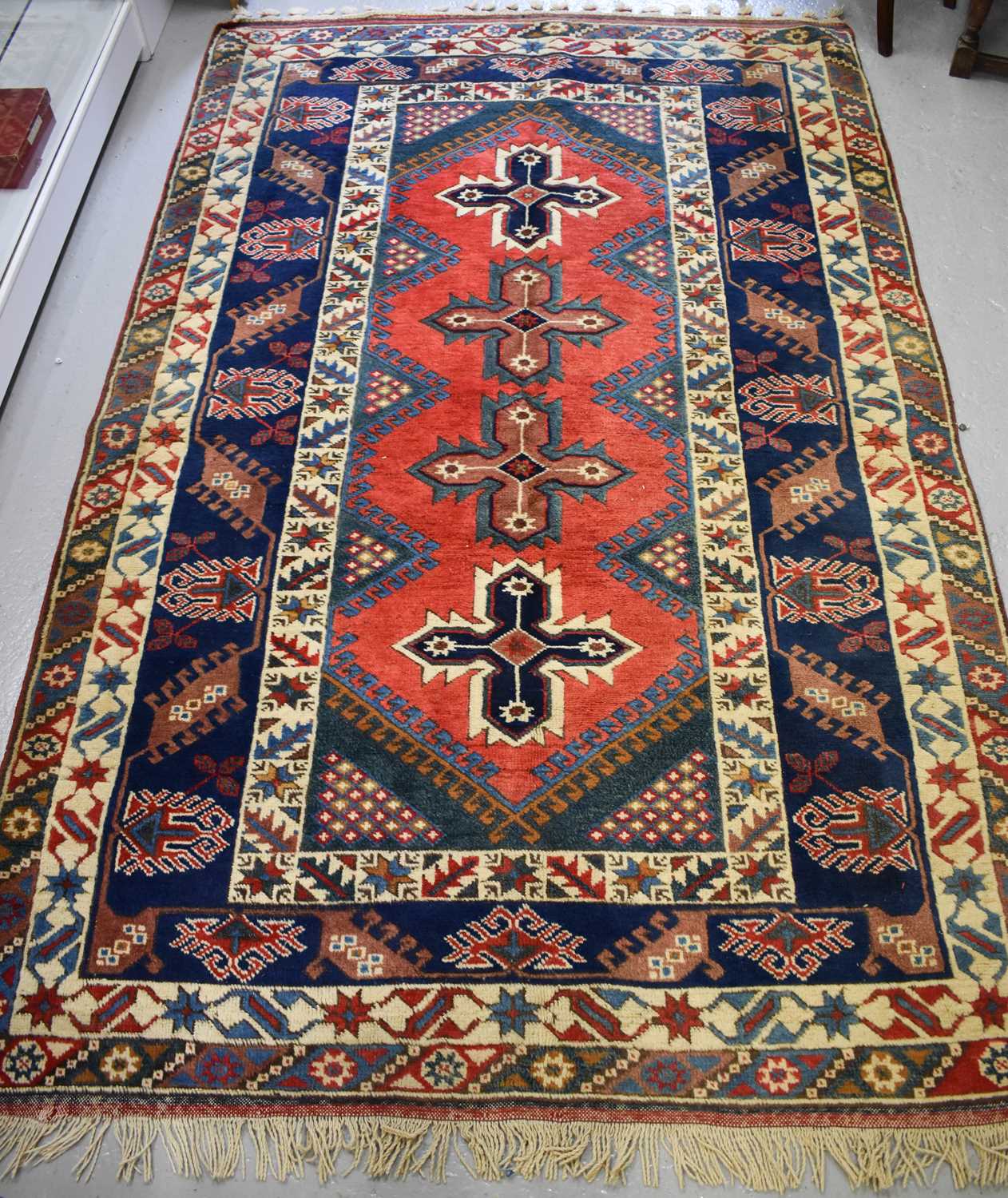 A Middle Eastern wool rug, with four stylised crosses to the red ground central panel, bordered by