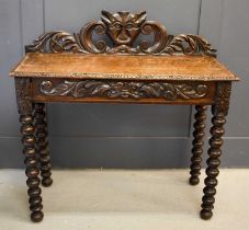 An oak 1930s silver table, the carved back depicting a face mask and scrollwork, with a frieze