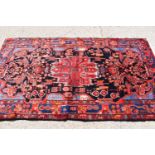 A Middle Eastern red ground wool rug, hand woven in deep pile, the centre depicting stylized figures